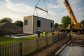 Crane lifting modular box over backyard fence